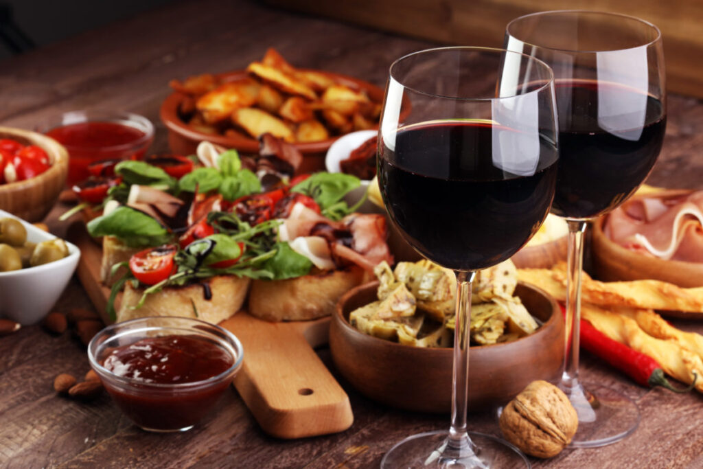 Italian antipasti wine snacks set. Cheese variety, Mediterranean olives, pickles, Prosciutto di Parma, tomatoes, artichokes and wine in glasses over black grunge background